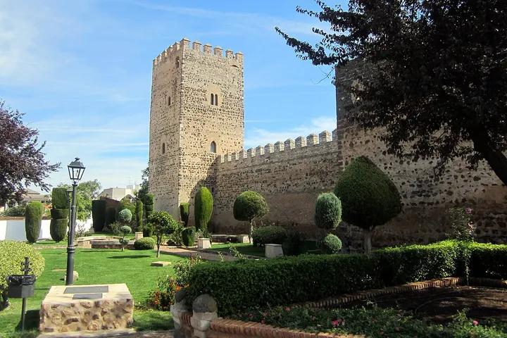 En primer plano, un jardín con un árbol, un farol y una fuente de piedra
