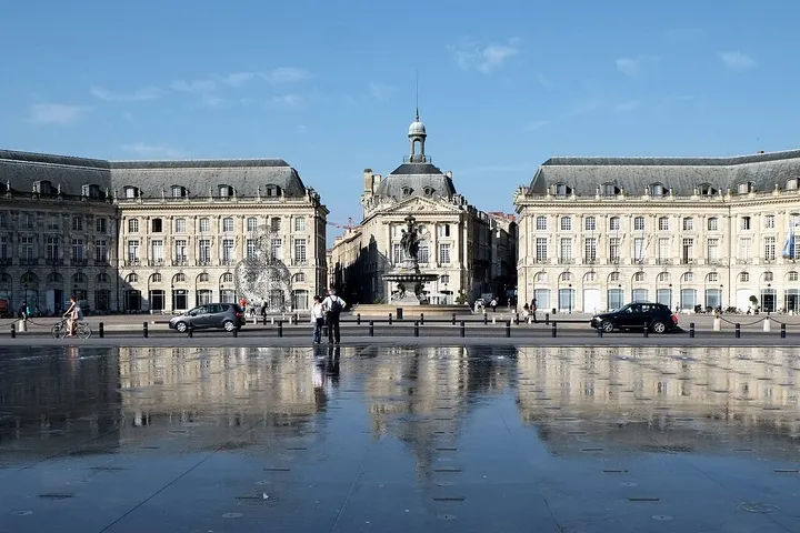 En primer plano, un gran espacio de agua, probablemente una plaza, con un edificio de estilo clásico a su lado