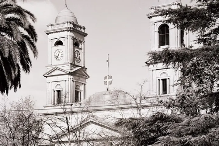En primer plano, un edificio con una torre con reloj y una cruz en el tejado