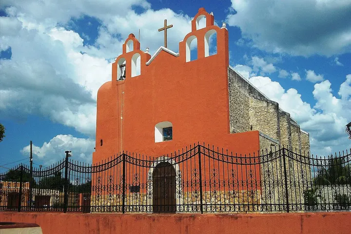 En primer plano, una iglesia de color rojo con dos cruces en la parte superior