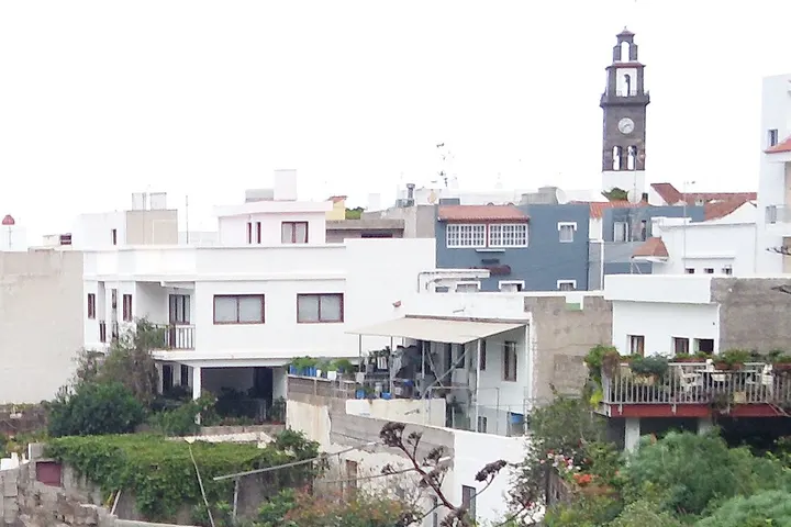 En primer plano, un edificio blanco con una entrada de garaje y una terraza con plantas