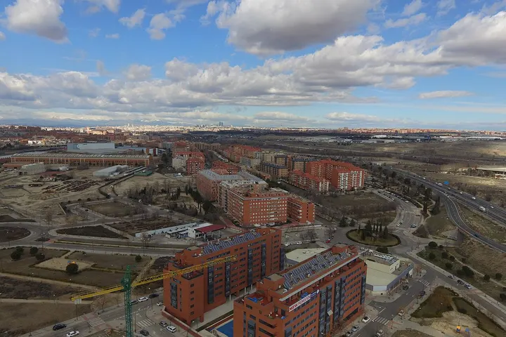 En primer plano, un edificio de apartamentos rojo con una piscina azul