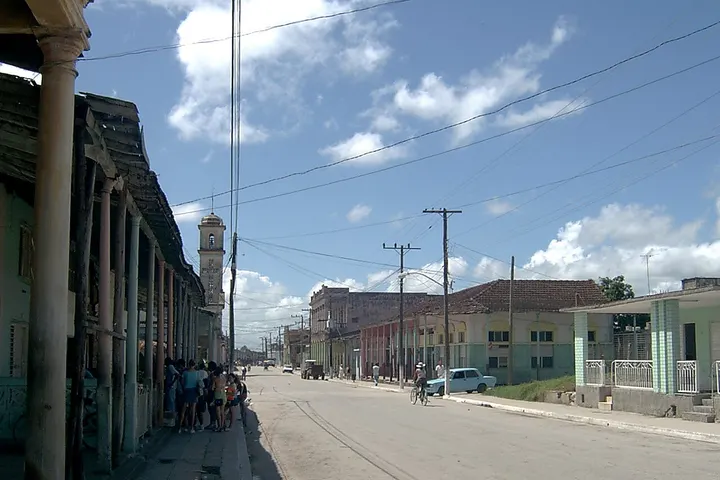 En primer plano, una calle con un edificio con un reloj de torre