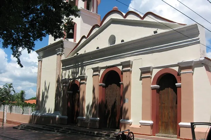 En primer plano, una iglesia blanca con arcos rojos y puertas de madera
