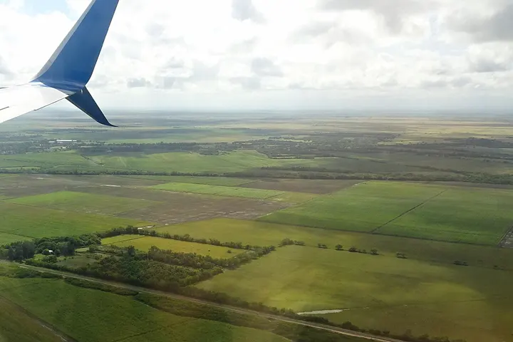 En primer plano, un avión sobrevuela un paisaje verde con campos y arboledas