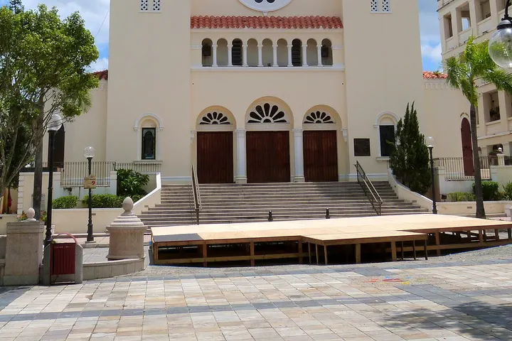 En primer plano, una plataforma de madera con escaleras que conduce a una iglesia blanca con puertas rojas