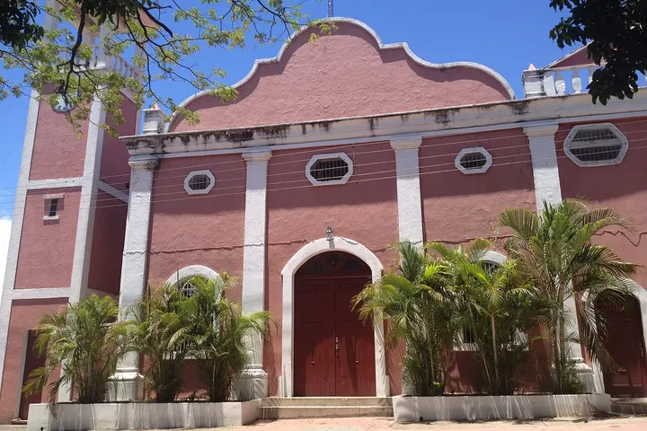 En primer plano, se ve un edificio rojo con un arco en la entrada y varios árboles alrededor