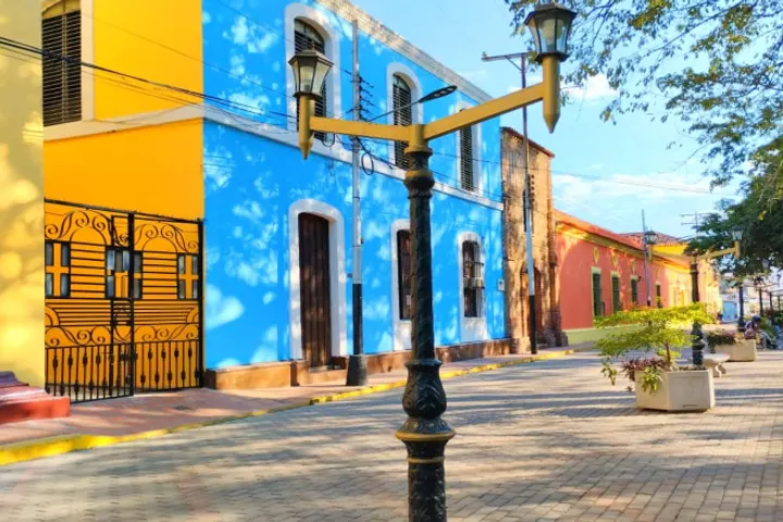 En primer plano, un edificio azul con una puerta y ventanas, rodeado de otros edificios de colores