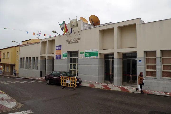 En primer plano, un edificio con una entrada y una puerta de vidrio, con un coche aparcado delante