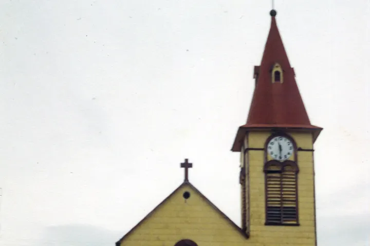 En primer plano, una torre de iglesia con un reloj y una cruz