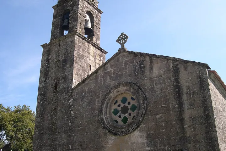 En primer plano, una iglesia con un campanario y una ventana con un rosetón