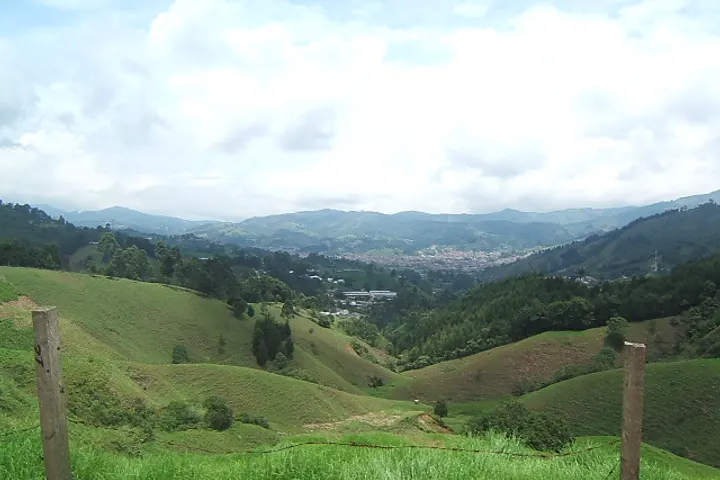 En primer plano, se ve una zona verde con un campo de pasto y una cerca de madera