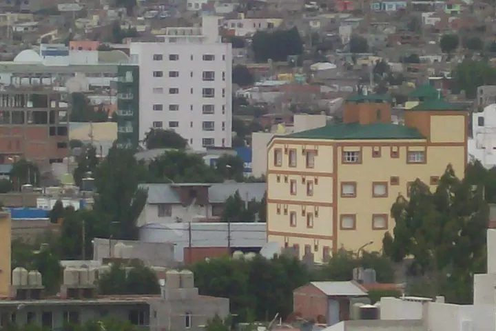 En primer plano, un edificio de color amarillo con un techo verde