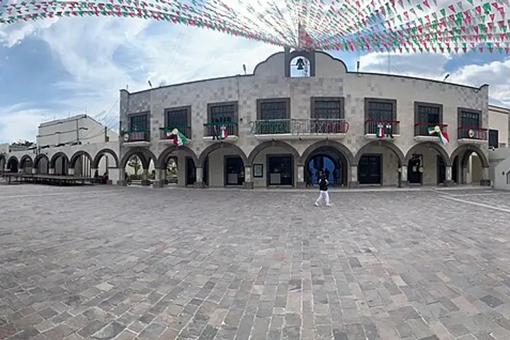 En primer plano, una plaza con un edificio de arcos y balcones, con banderas colgando en el cielo