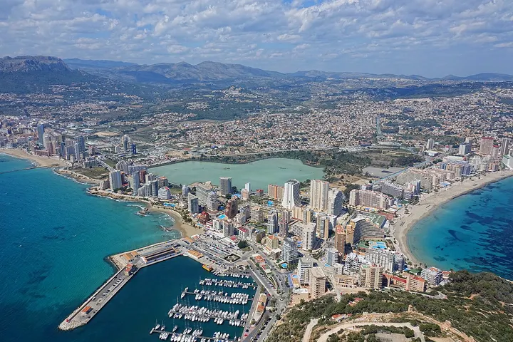 En primer plano, se ve un puerto con barcos y un gran complejo de edificios de apartamentos y hoteles