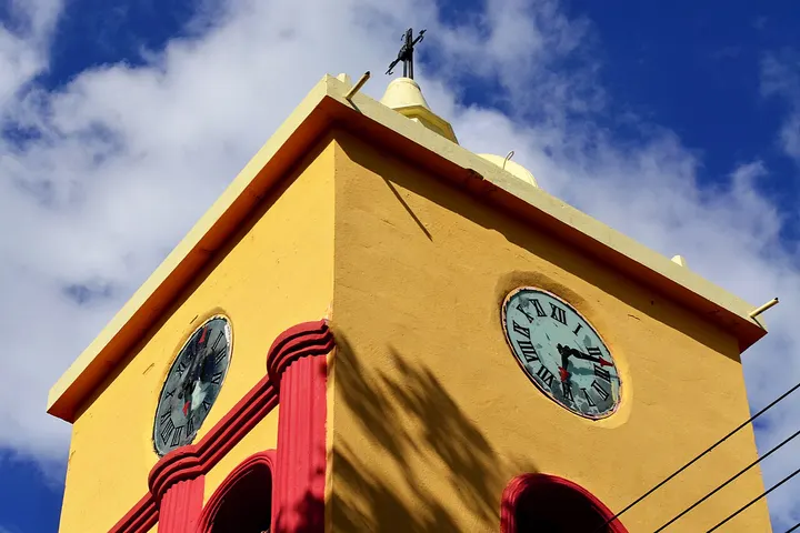 En primer plano, dos relojes en un edificio amarillo con arcos rojos