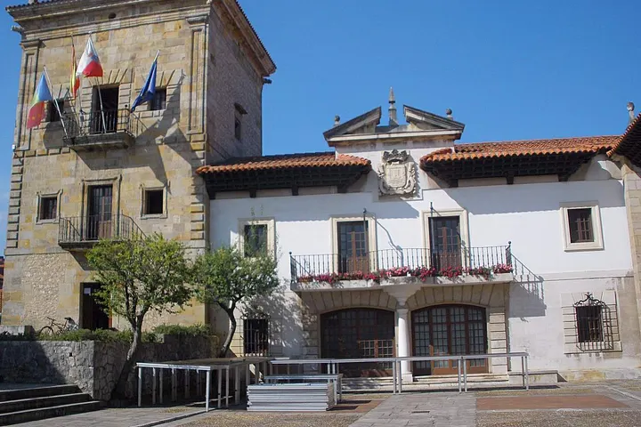 En primer plano, una estructura blanca con balcones y una entrada con rejas