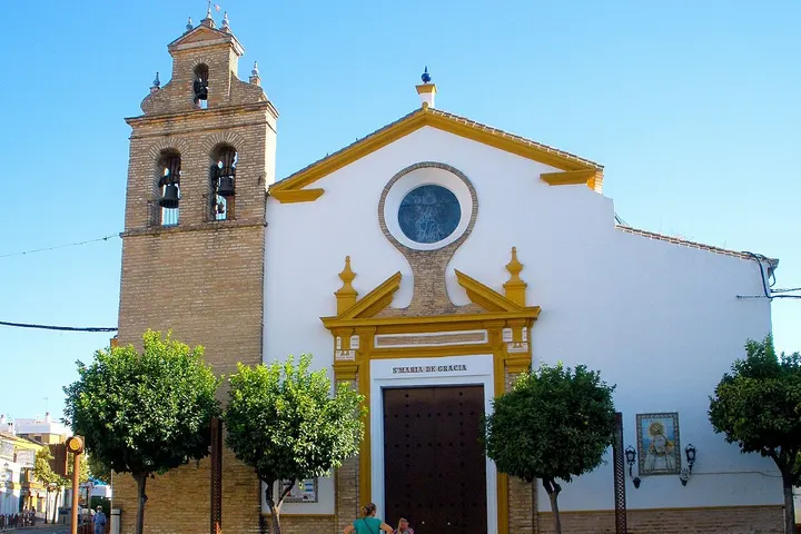 En primer plano, una iglesia con una torre de campanario y una puerta con un gran dintel y un óculo