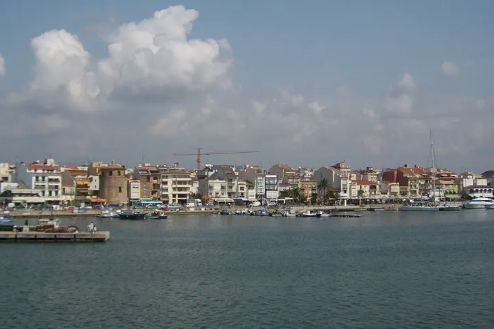 En primer plano, un lago con barcos y una ciudad con edificios de varios pisos