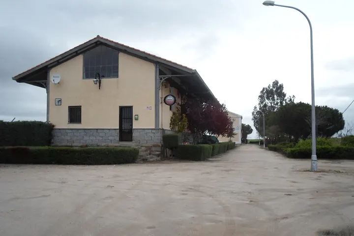 Un edificio de dos plantas con un techo inclinado, rodeado de árboles y una calle con una farola