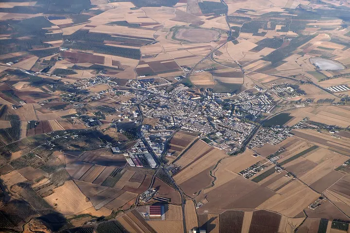 En primer plano, un gran campo de cultivo rodea un pueblo de casas blancas y edificios industriales
