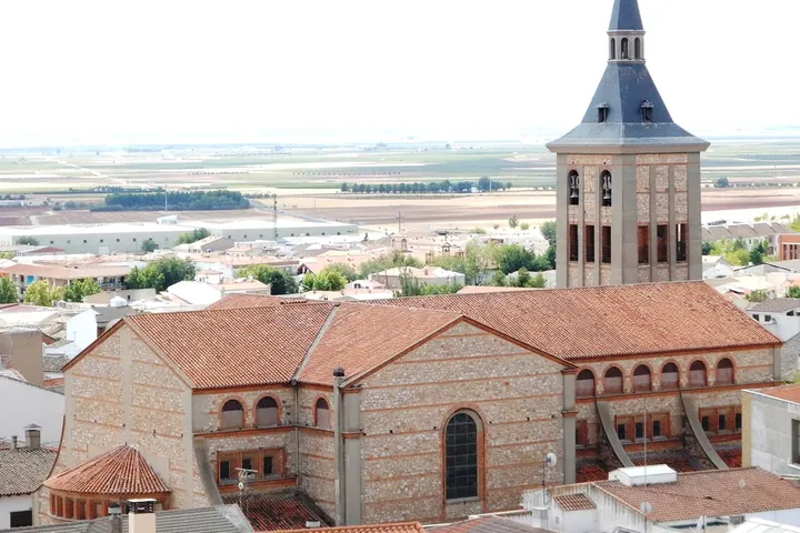 En primer plano, una iglesia de piedra con un campanario de ladrillo y una torre de piedra