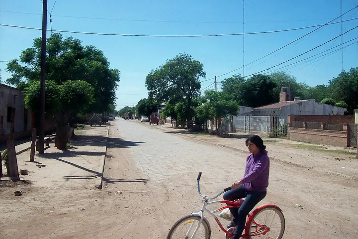 En primer plano, una mujer monta una bicicleta roja en una calle de una ciudad con un cielo azul