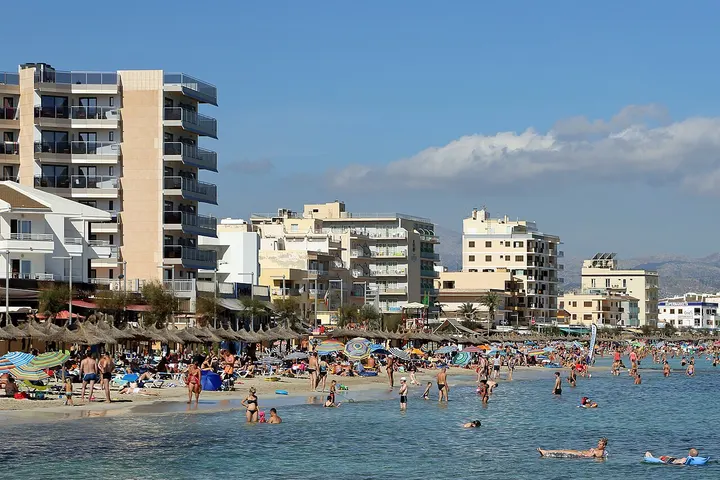 En primer plano, una playa con gente nadando y sentada en sillas de playa