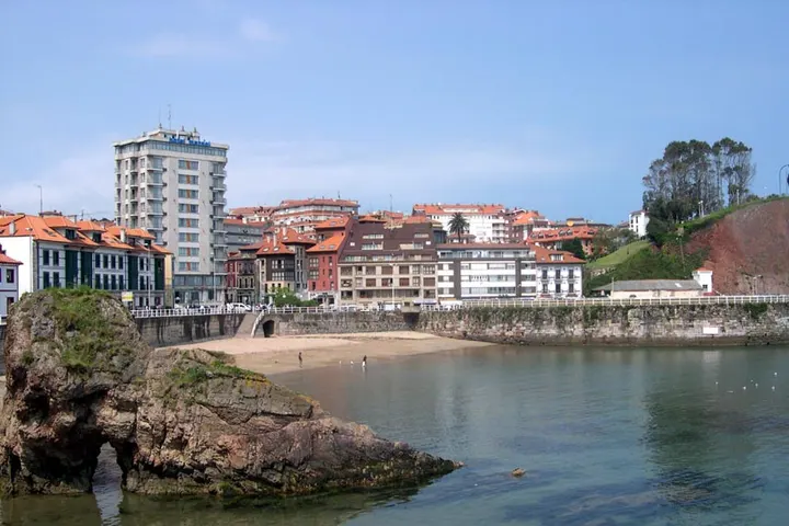 En primer plano, una playa con un gran roca en la orilla