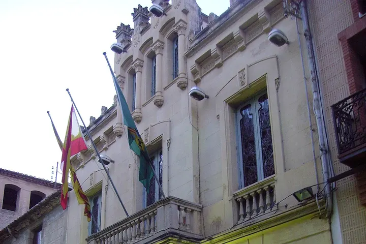 En primer plano, un edificio con una serie de banderas de colores en su fachada
