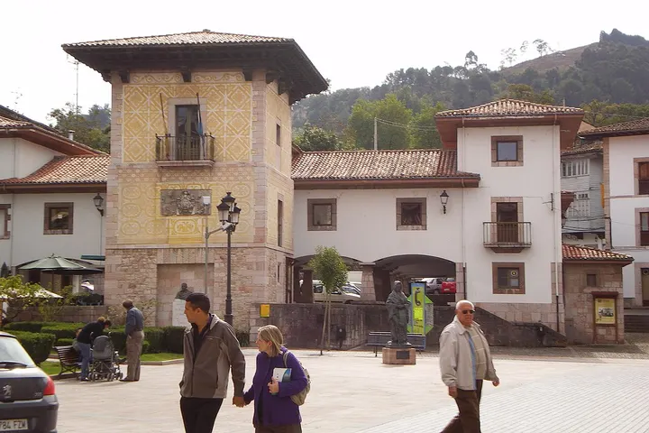 En primer plano, una pareja de jóvenes camina por una plaza con un edificio de estilo tradicional en el fondo