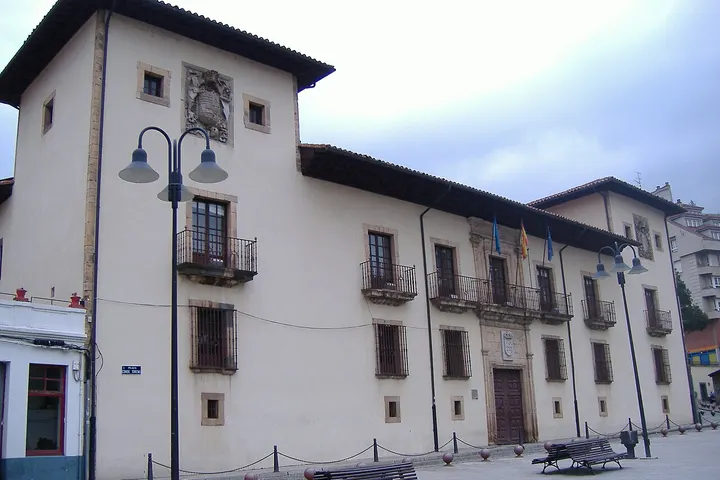 En primer plano, una casa blanca con balcones y ventanas, con una calle vacía y una farola