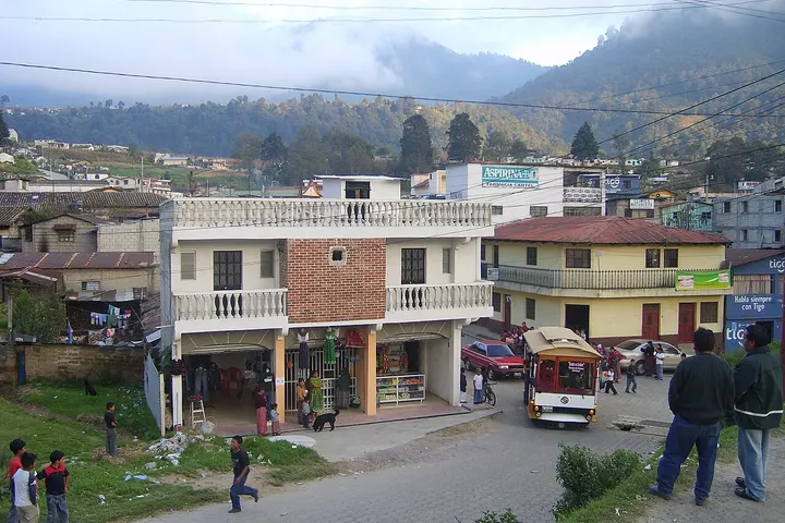 En primer plano, una casa de dos pisos con balcones y un trolebús en la calle