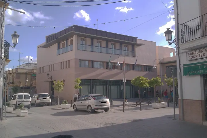 En primer plano, un edificio de dos plantas con balcones en la parte superior, con un coche aparcado delante