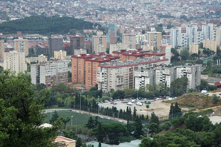 En primer plano, un campo de fútbol rodeado de árboles y edificios de apartamentos