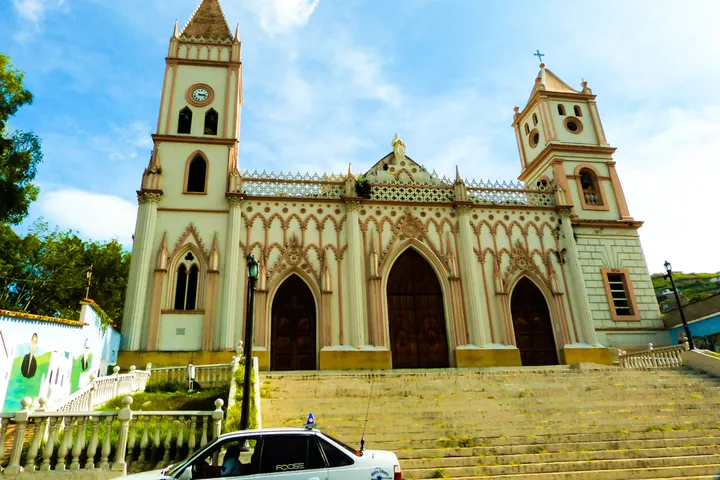 En primer plano, un coche policial está estacionado frente a una iglesia con una torre y un campanario