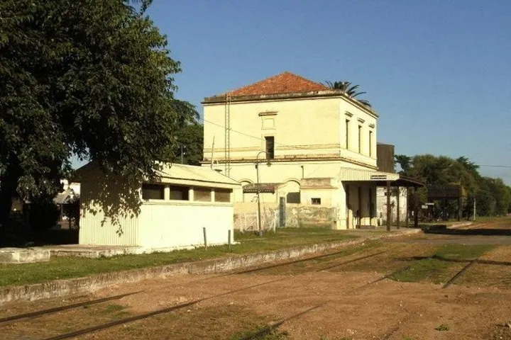 En primer plano, una casa de dos pisos con un tejado rojo, rodeada por árboles y una calle de tierra