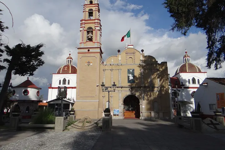 La iglesia de San Miguel Arcángel, con su torre y bandera mexicana, es el edificio más destacado en primer plano