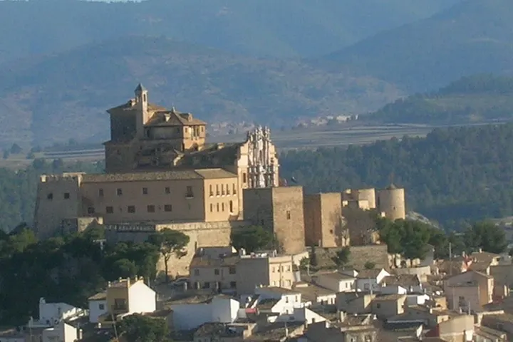 En primer plano, una torre de un castillo, con un edificio grande y otro más pequeño en el centro