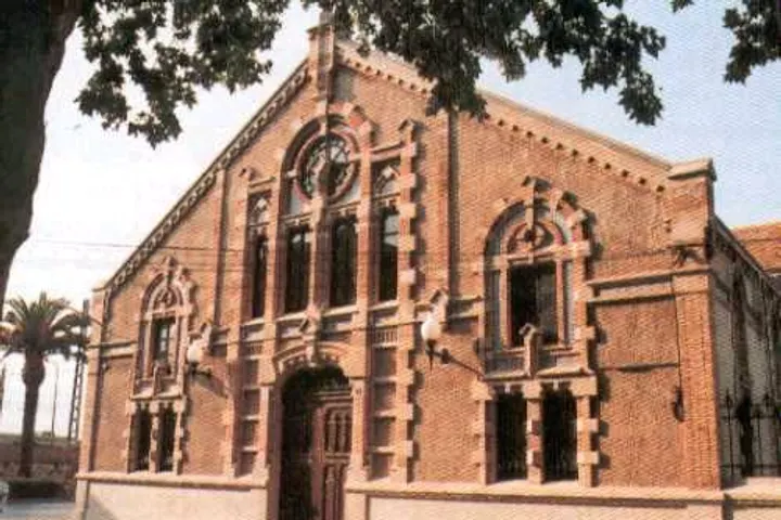 En primer plano, una sinagoga de ladrillo rojo con arcos y ventanas adornadas
