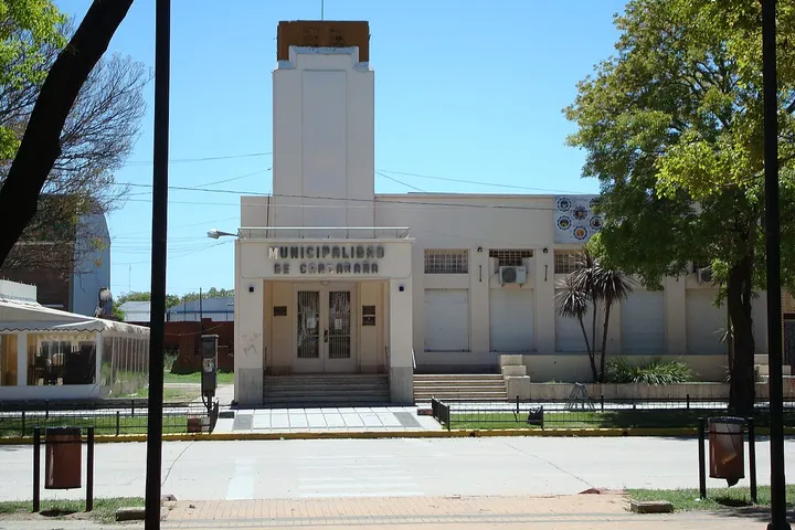 En primer plano, se ve un edificio municipal con una torre y una entrada principal