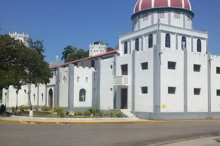 En primer plano, una iglesia blanca con una torre redonda y una cúpula roja