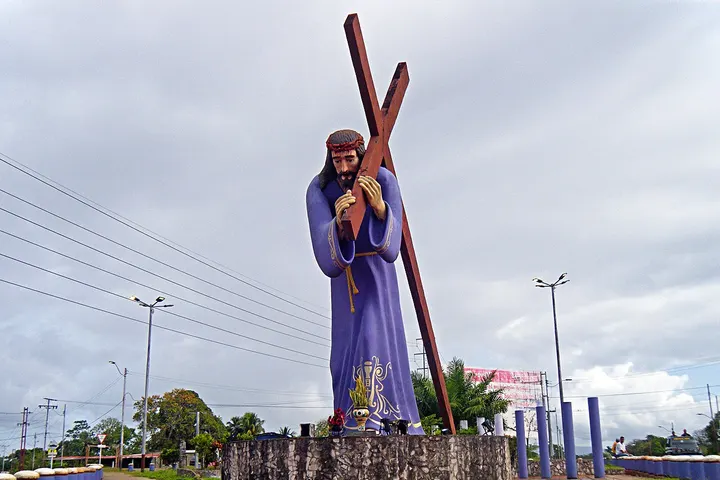 En primer plano, una estatua de Jesús de Nazaret con una cruz en la mano