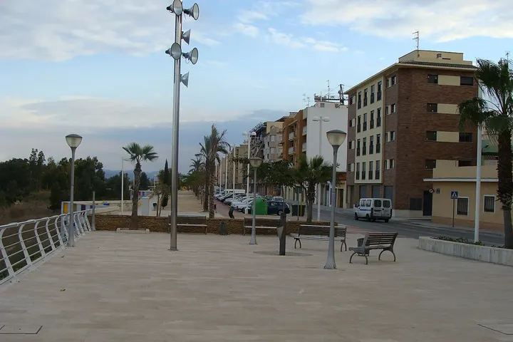 En primer plano, se ve una plaza con bancos y farolas