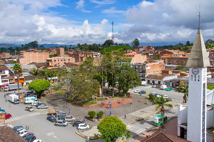 En primer plano, una iglesia con campanario y reloj, rodeada de árboles y un parque
