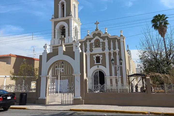 En primer plano, una iglesia con una torre y un portal de hierro forjado
