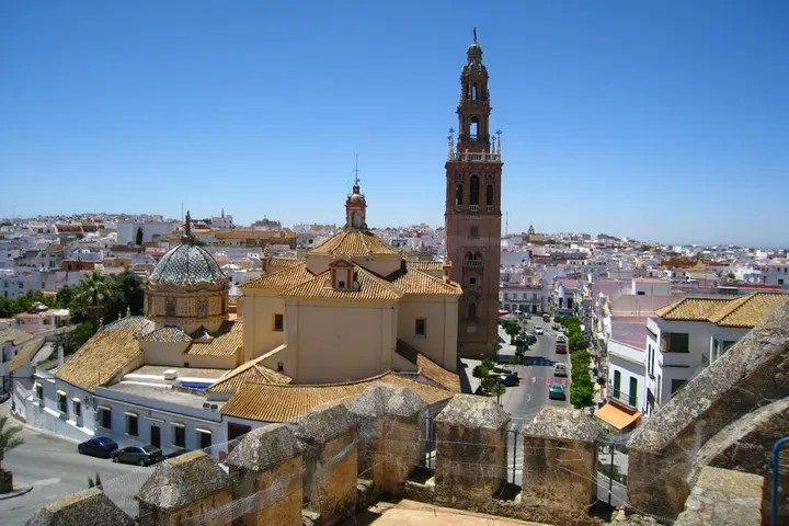 En primer plano, un campanario de una iglesia con una torre de reloj y una cúpula de azulejos