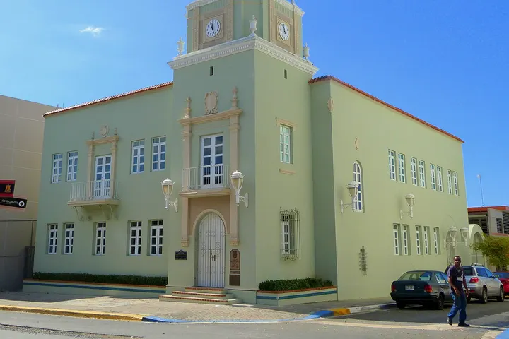 En primer plano, una edificación de estilo clásico con un reloj en su torre