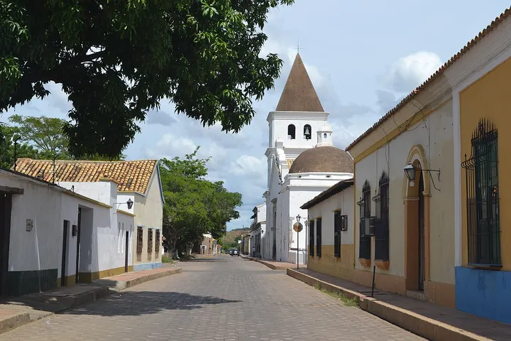 En primer plano, una calle adoquinada con casas de colores y una iglesia blanca con torre