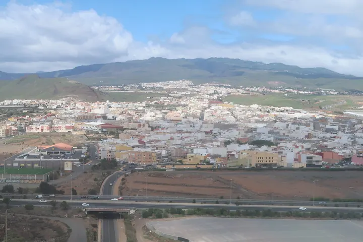 En primer plano, una carretera con un puente sobre un canal, rodeada de edificios y casas blancas